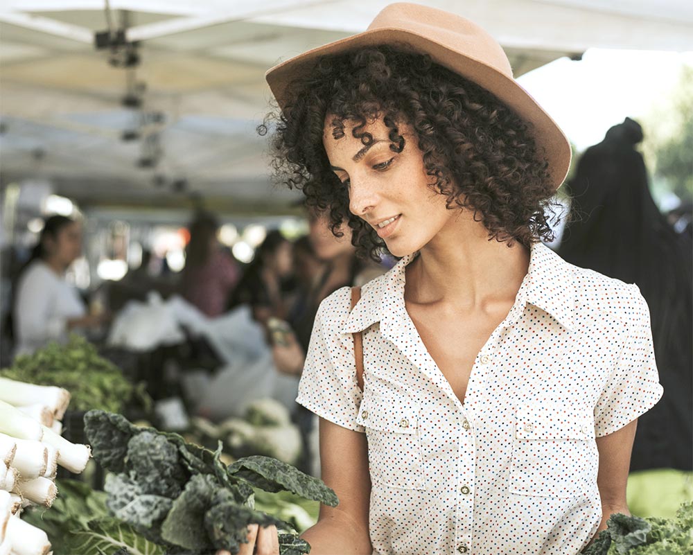 A young lady at a farmers' market holding a bunch of kale